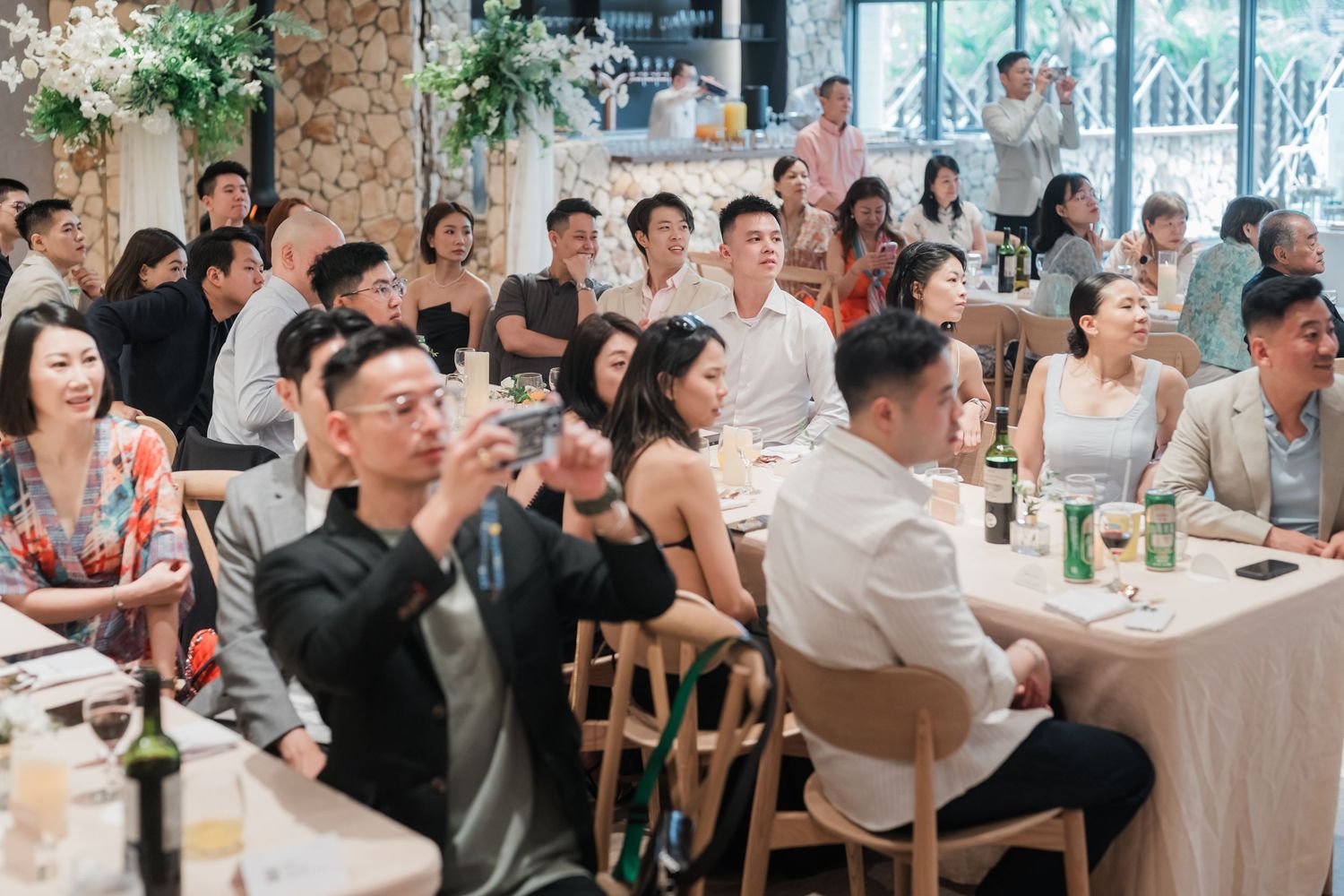 Large group of people sitting at long tables in a busy restaurant or dining hall interior.
