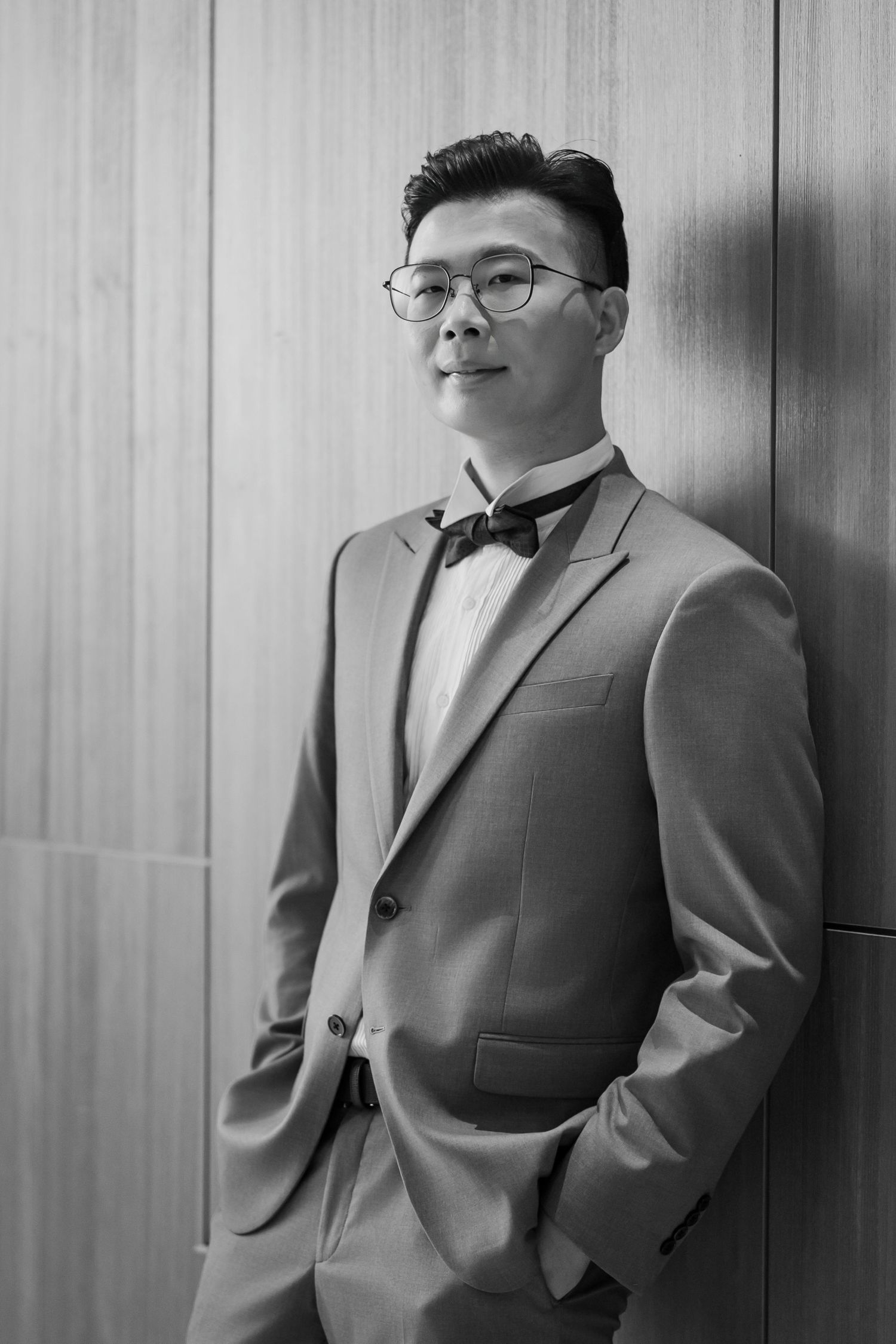 Black and white portraits of a person in formal attire showing three different poses against a paneled wall.
