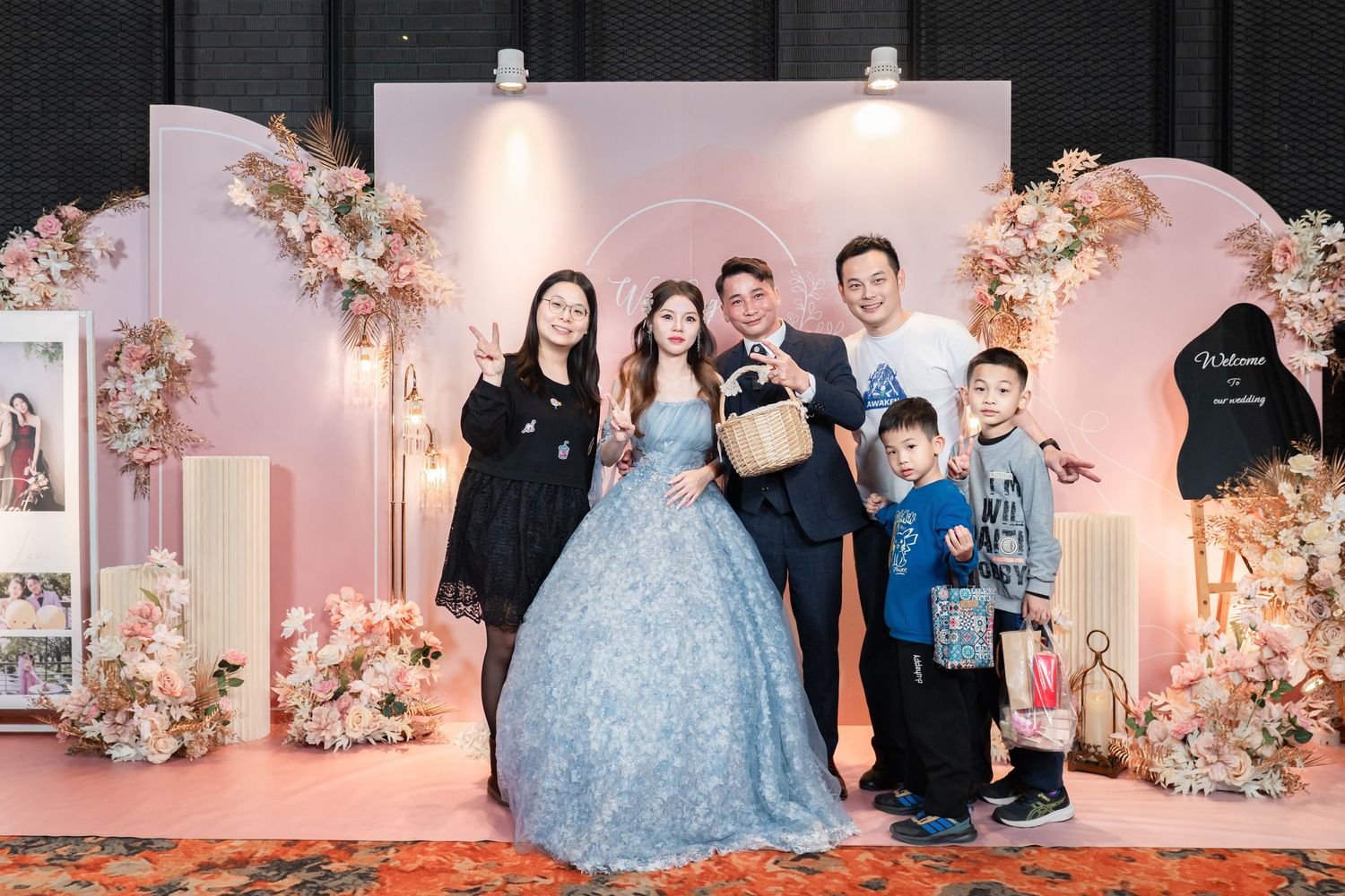 A wedding celebration setup with pink floral decorations and a light blue gown against a blush pink backdrop.