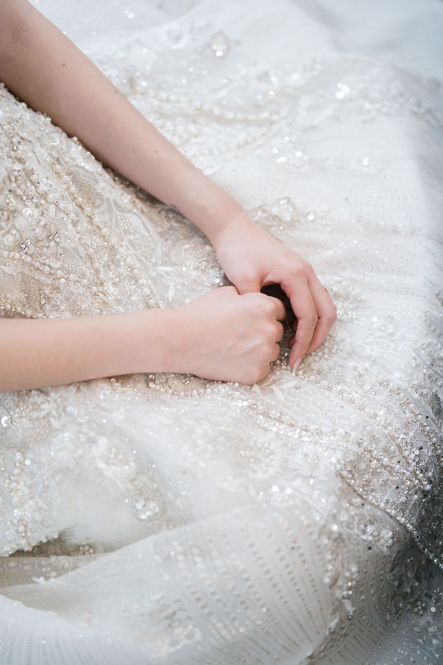 Close-up of hands touching an elegant white beaded and sequined wedding dress fabric with delicate embellishments.