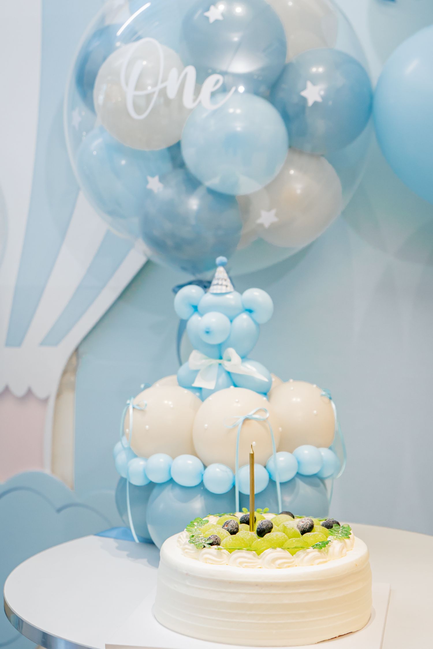Light blue and white balloon decorations with a white birthday cake topped with cloud decorations create a dreamy party setup.