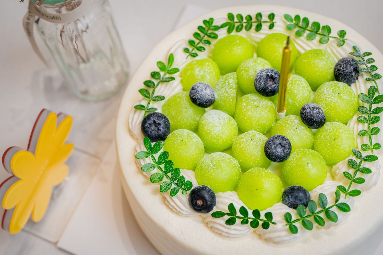 Green grapes and blueberries arranged in a decorative pattern with delicate leaf garnishes on a white plate.