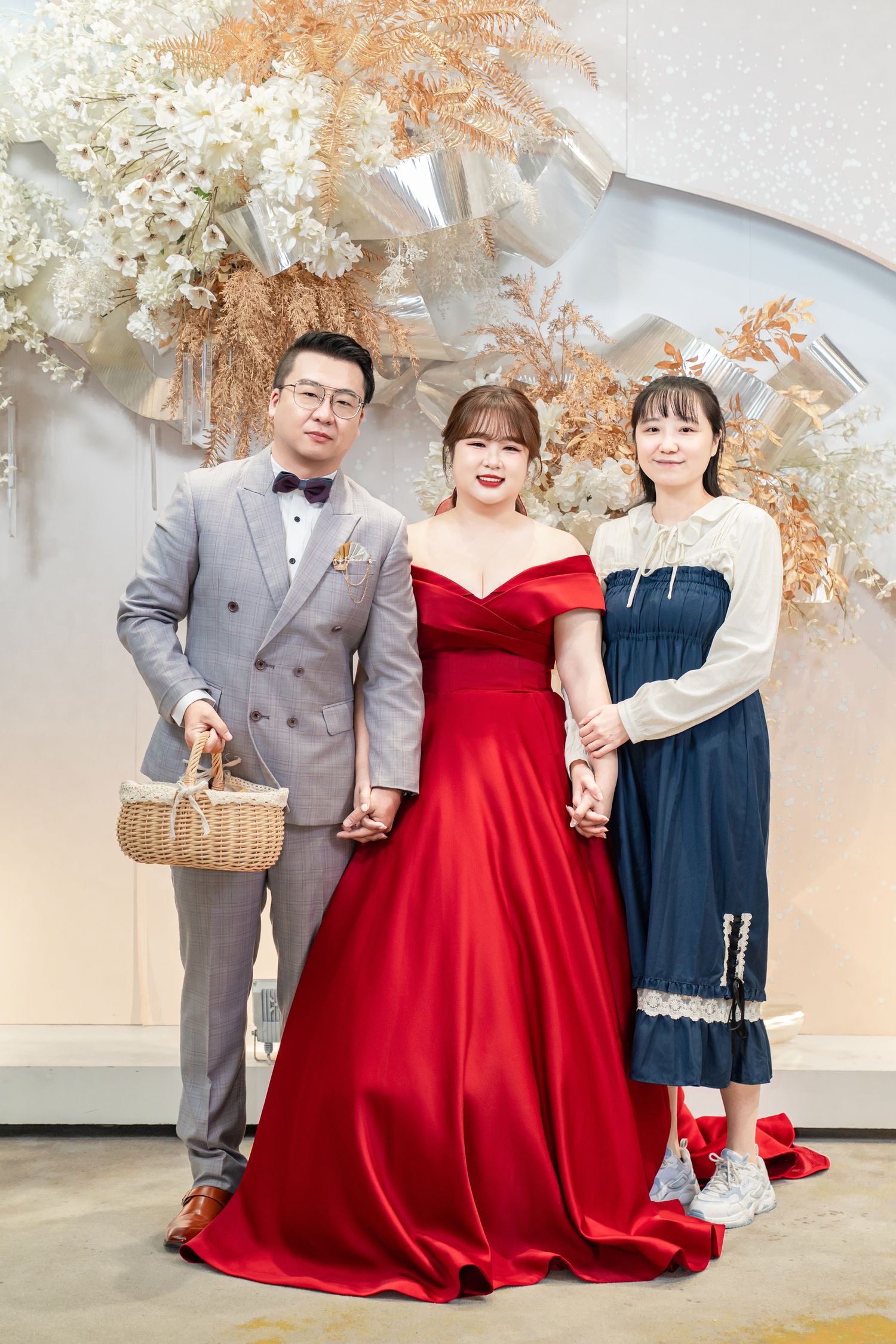 A group poses together in formal attire including a red gown and navy dress against a light floral backdrop.