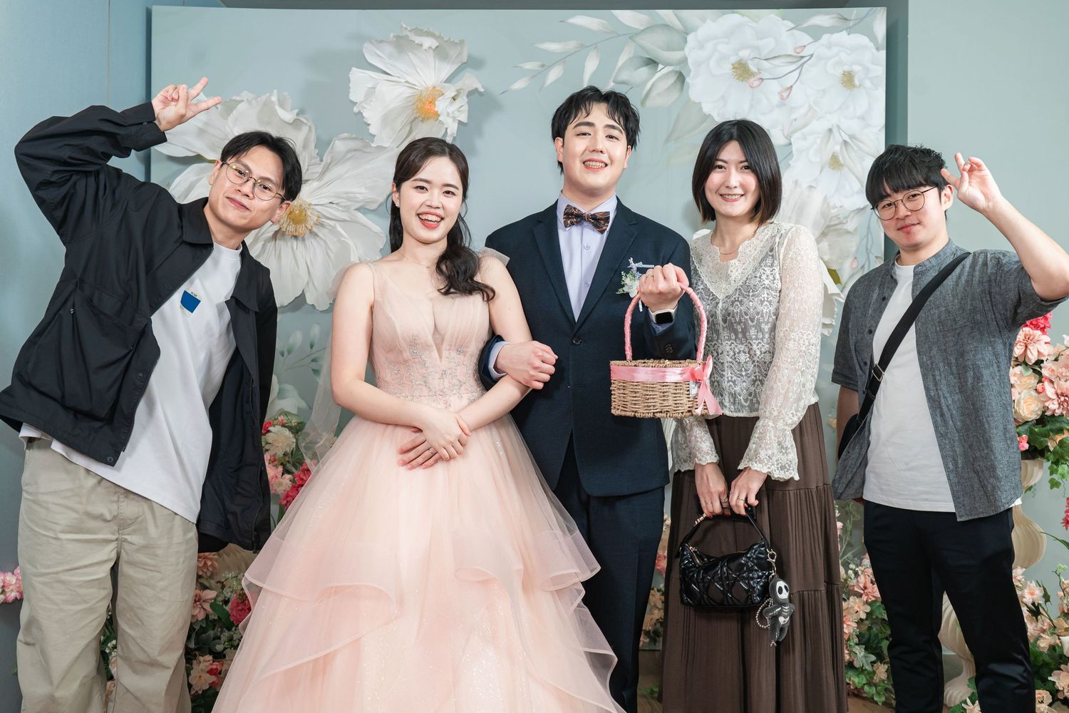 Wedding couple and friends pose casually in front of a floral backdrop at a celebration.