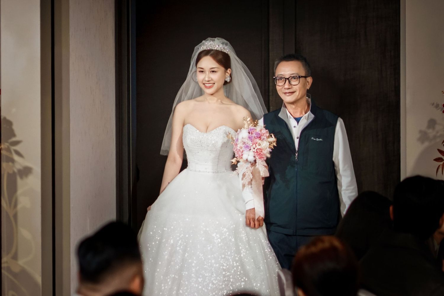 A bride in a white lace wedding dress poses with a companion in a dark hallway.