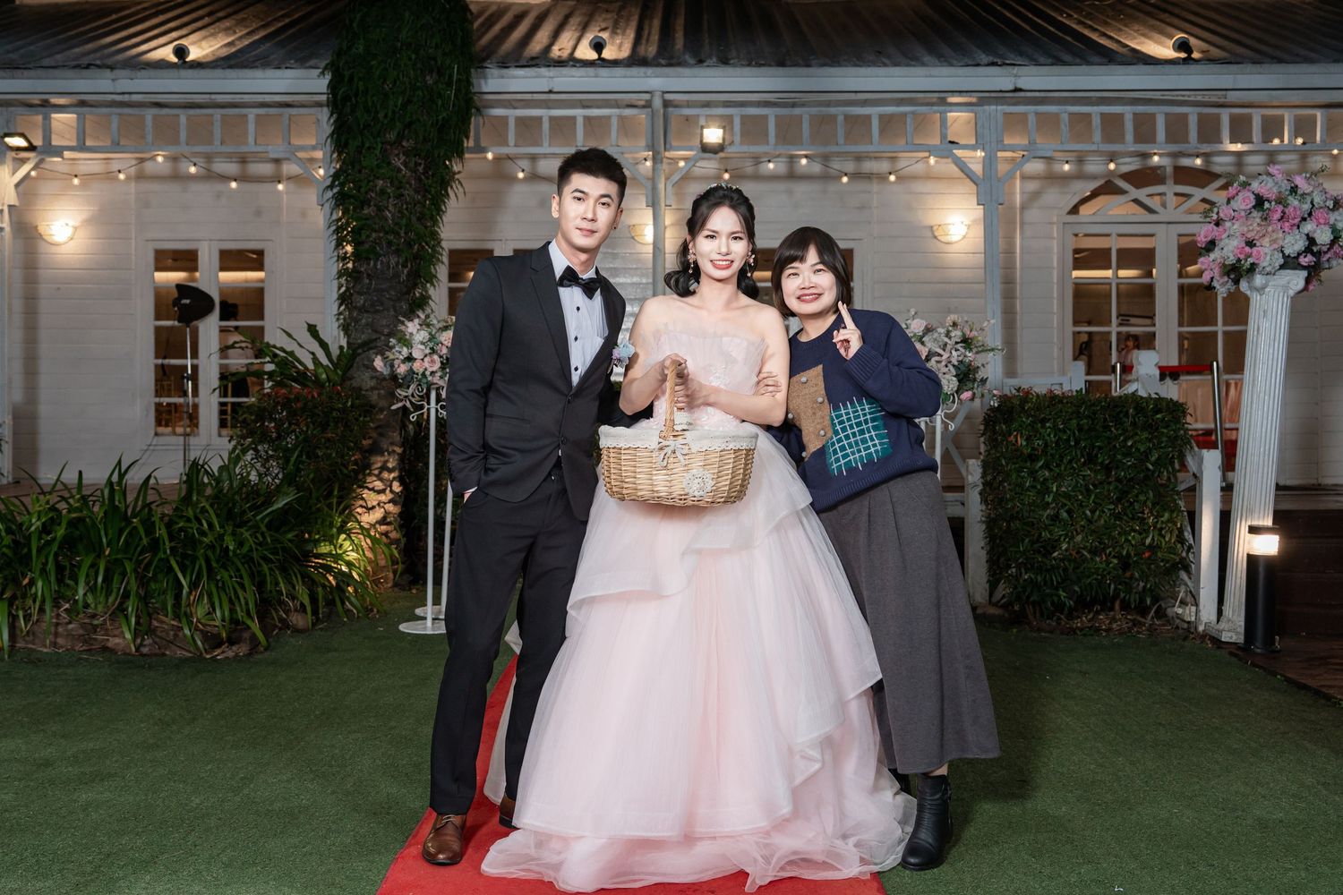 Wedding party poses for formal photos at an elegant venue with string lights and greenery decorations.