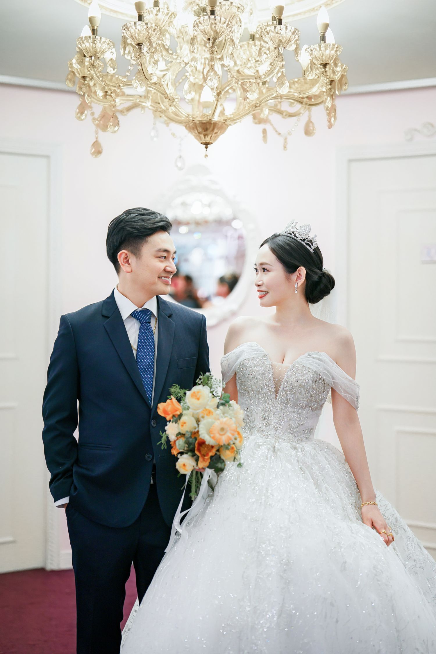A couple shares a joyful moment in an elegant ballroom with crystal chandeliers during their wedding celebration.