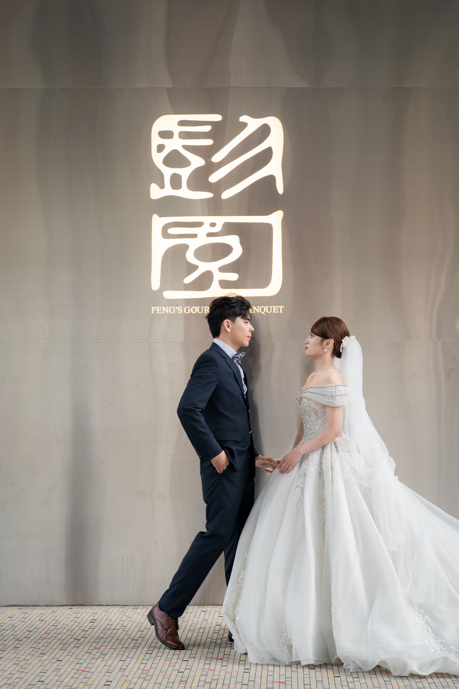 Elegant couple in wedding attire posing at Feng's Odeum Banquet venue, groom in navy suit, bride in white gown.