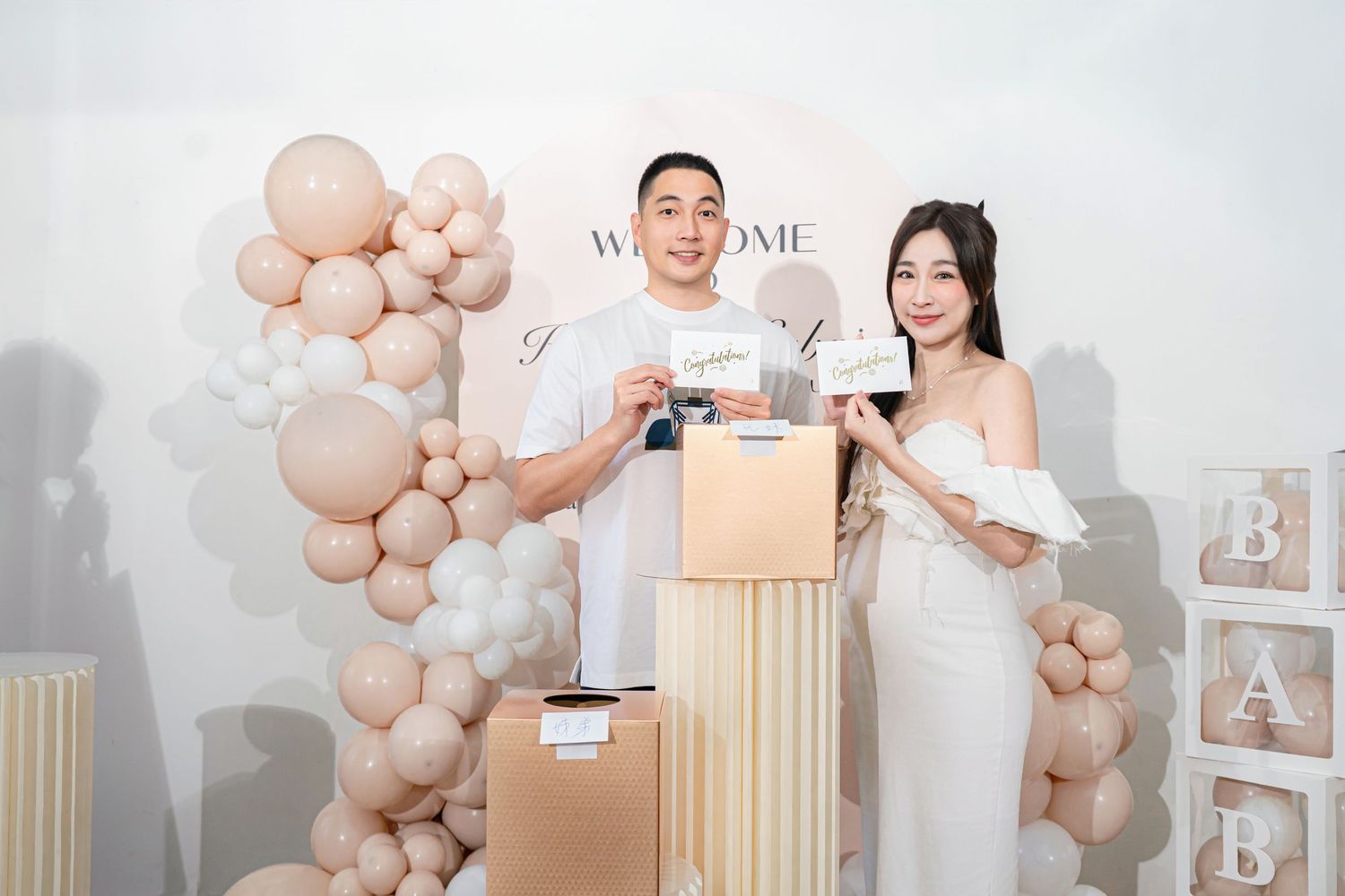 A couple celebrates with wine glasses in front of beige balloon arch decorations and elegant column displays.