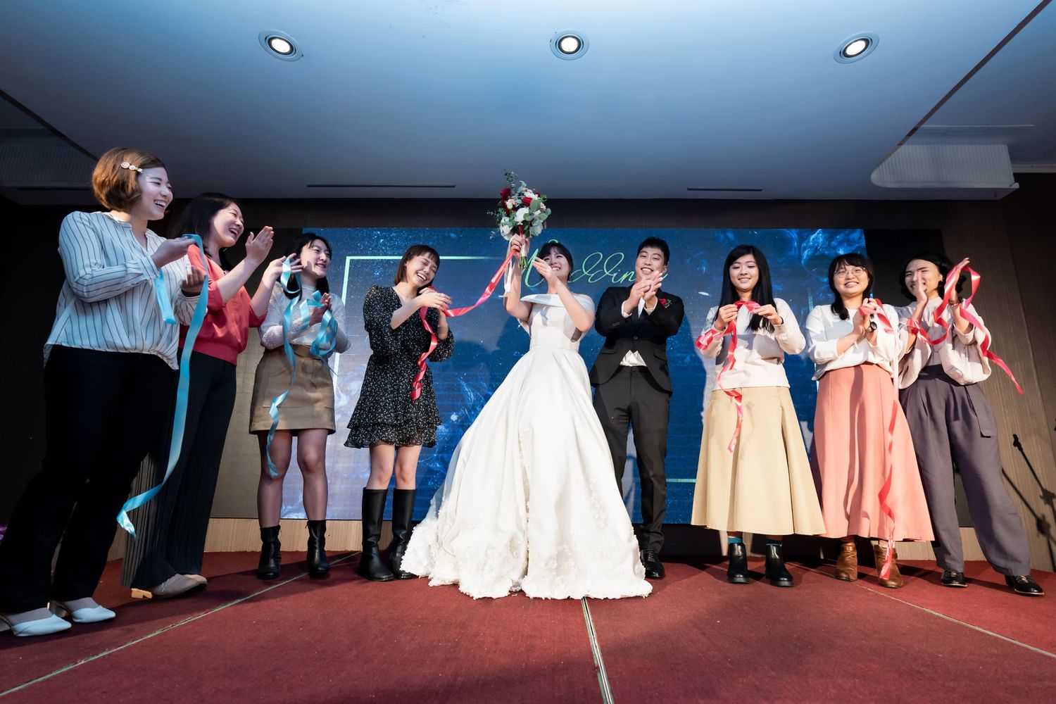 Wedding celebration on red carpet with guests participating in a group activity.