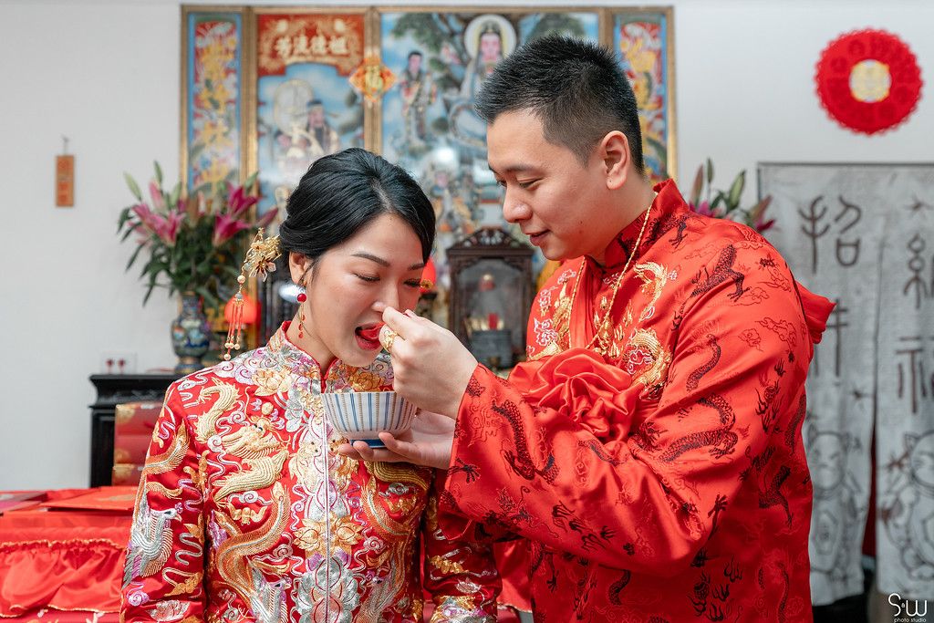 Traditional tea ceremony with couple in matching red Chinese wedding attire.