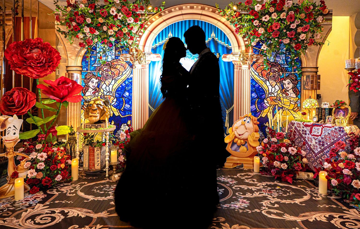 Silhouetted couple embracing in Beauty and the Beast themed wedding backdrop with roses and stained glass.