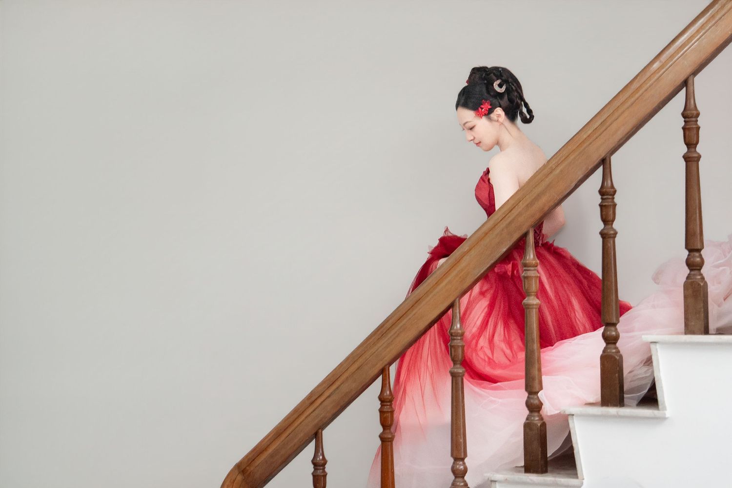 Woman in elegant red Hanfu dress descending wooden staircase, smiling gracefully in traditional Chinese attire.