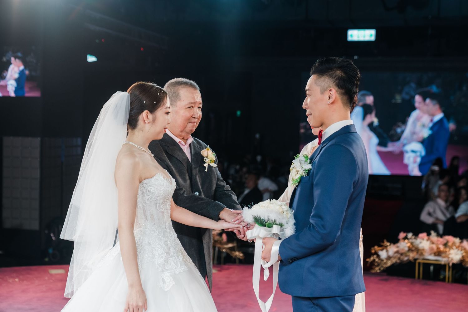 A wedding ceremony takes place on a stage with bright lights and decor as participants interact during the service.