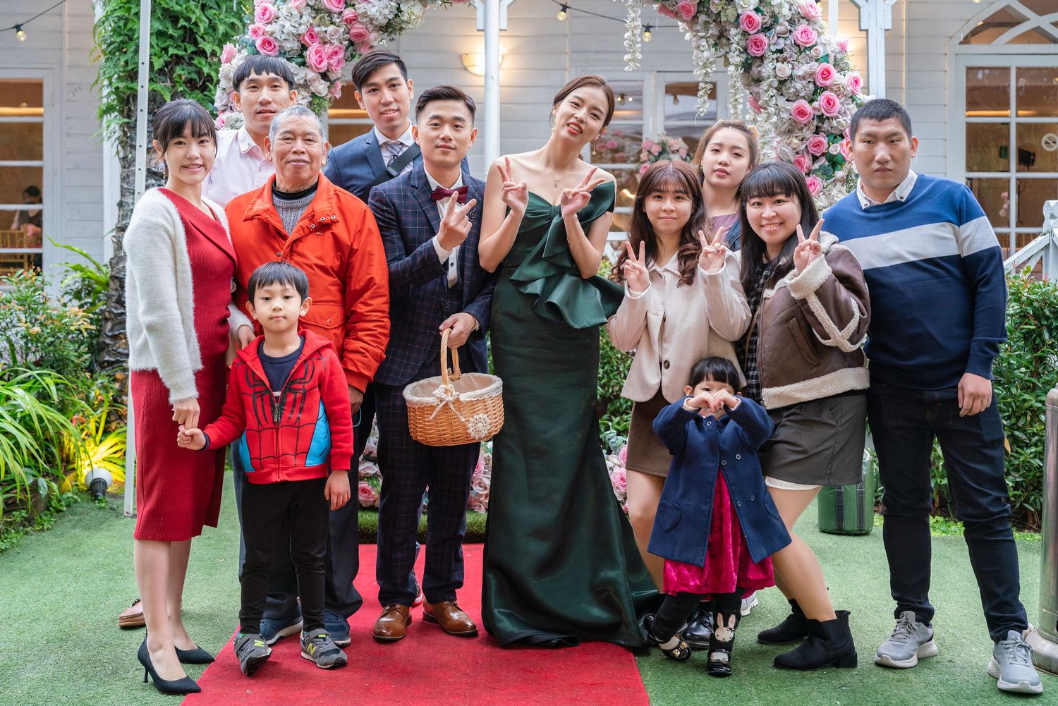 A group photo of people standing together at an event under a floral arch on a red carpet.