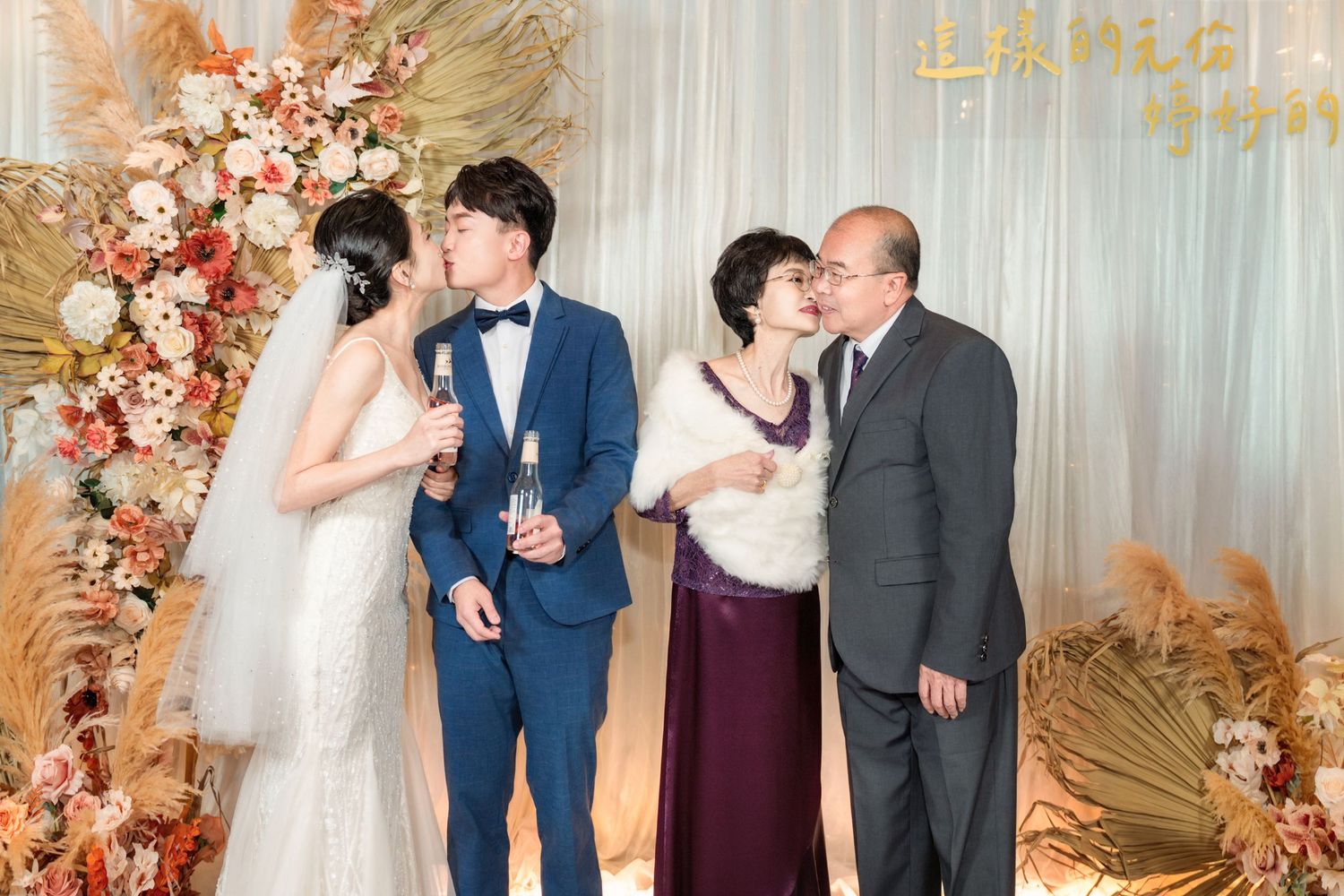 Wedding celebration with couples posing by an elegant floral arch with peach roses and dried palm fronds.