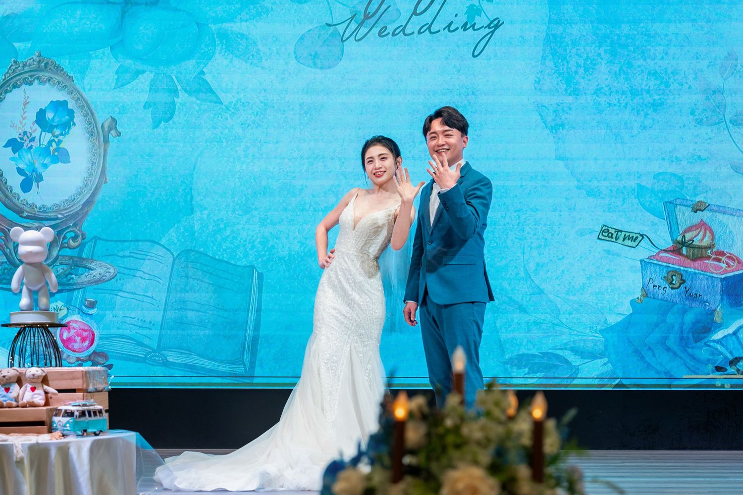 A wedding celebration with a bright turquoise backdrop featuring decorative elements and floral arrangements.