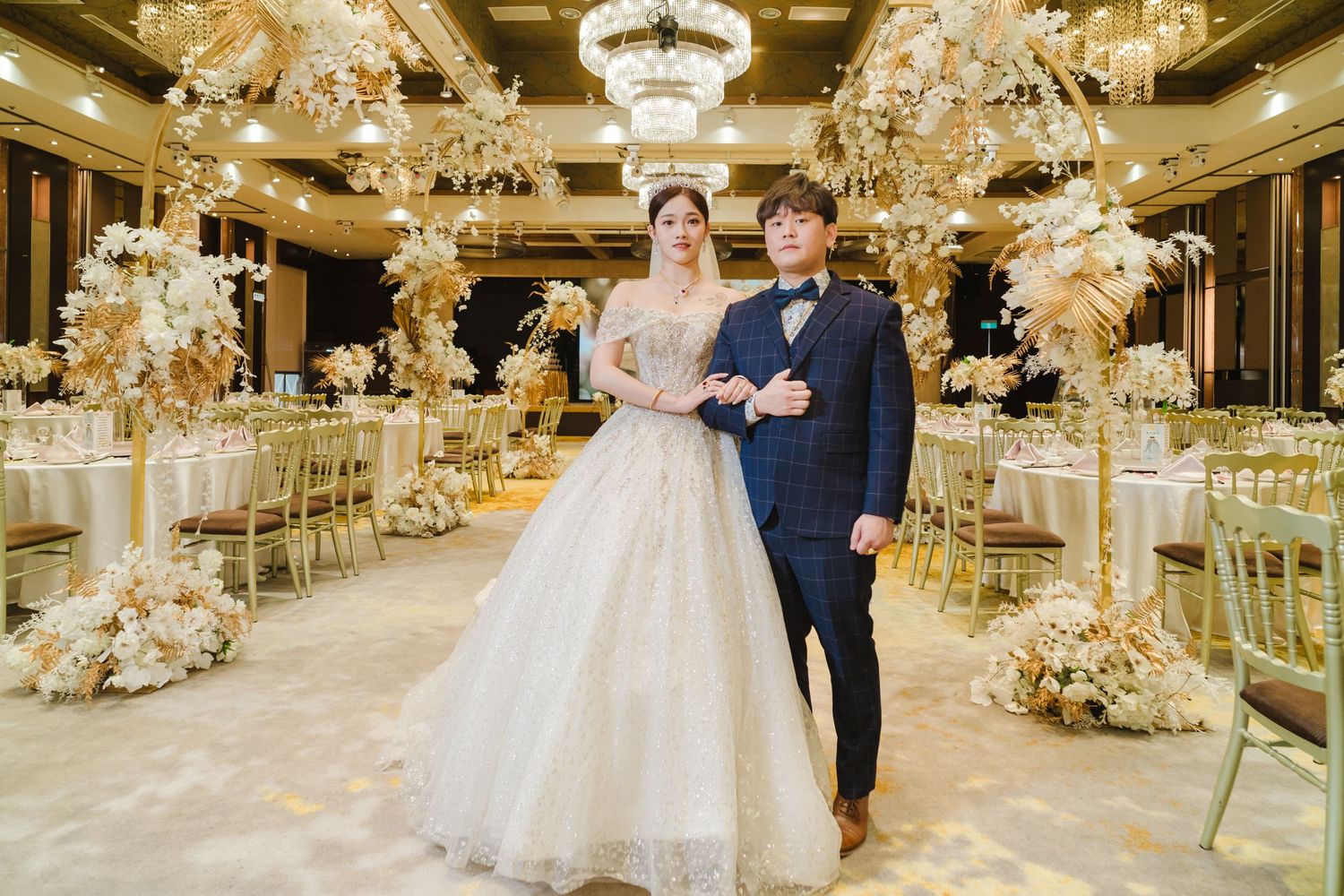 Elegant wedding reception venue decorated with crystal chandeliers and golden floral arrangements in a luxurious ballroom.