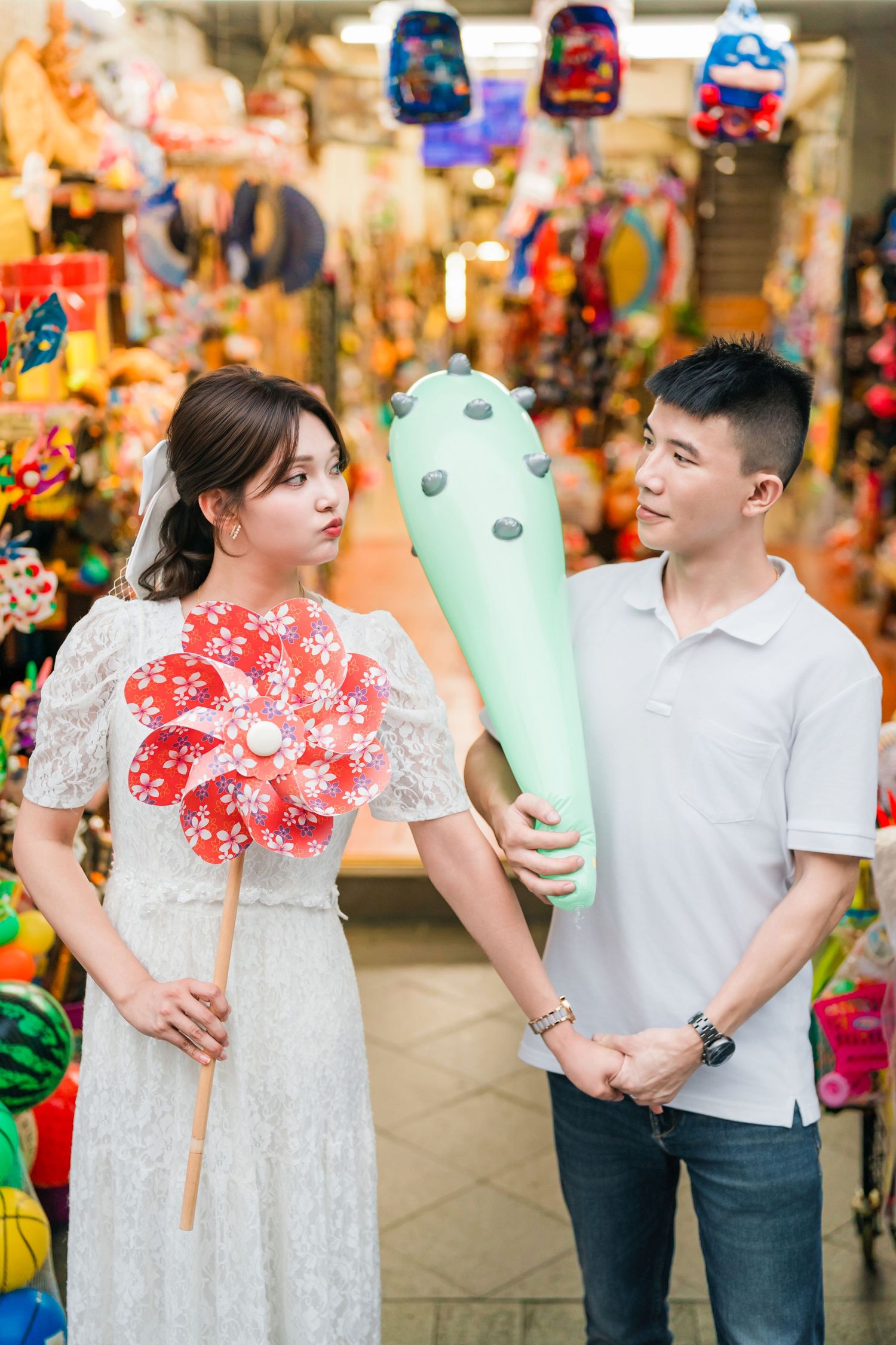 A couple poses with a mint green plush toy in front of a colorful carnival game booth display.