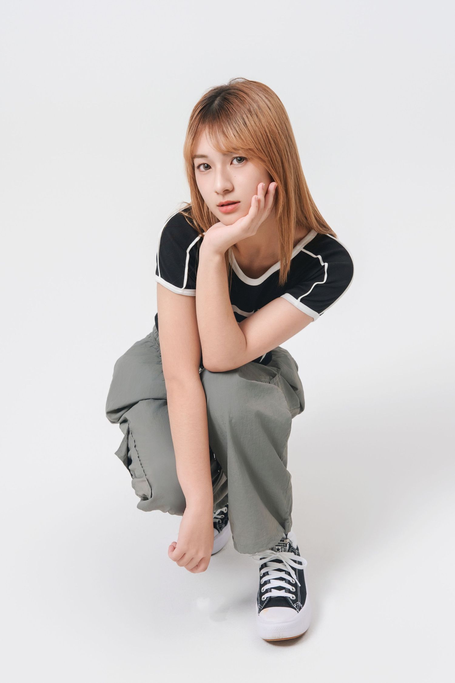 A person in a gray sweater and sneakers crouches in various poses against a white backdrop for a fashion photoshoot.