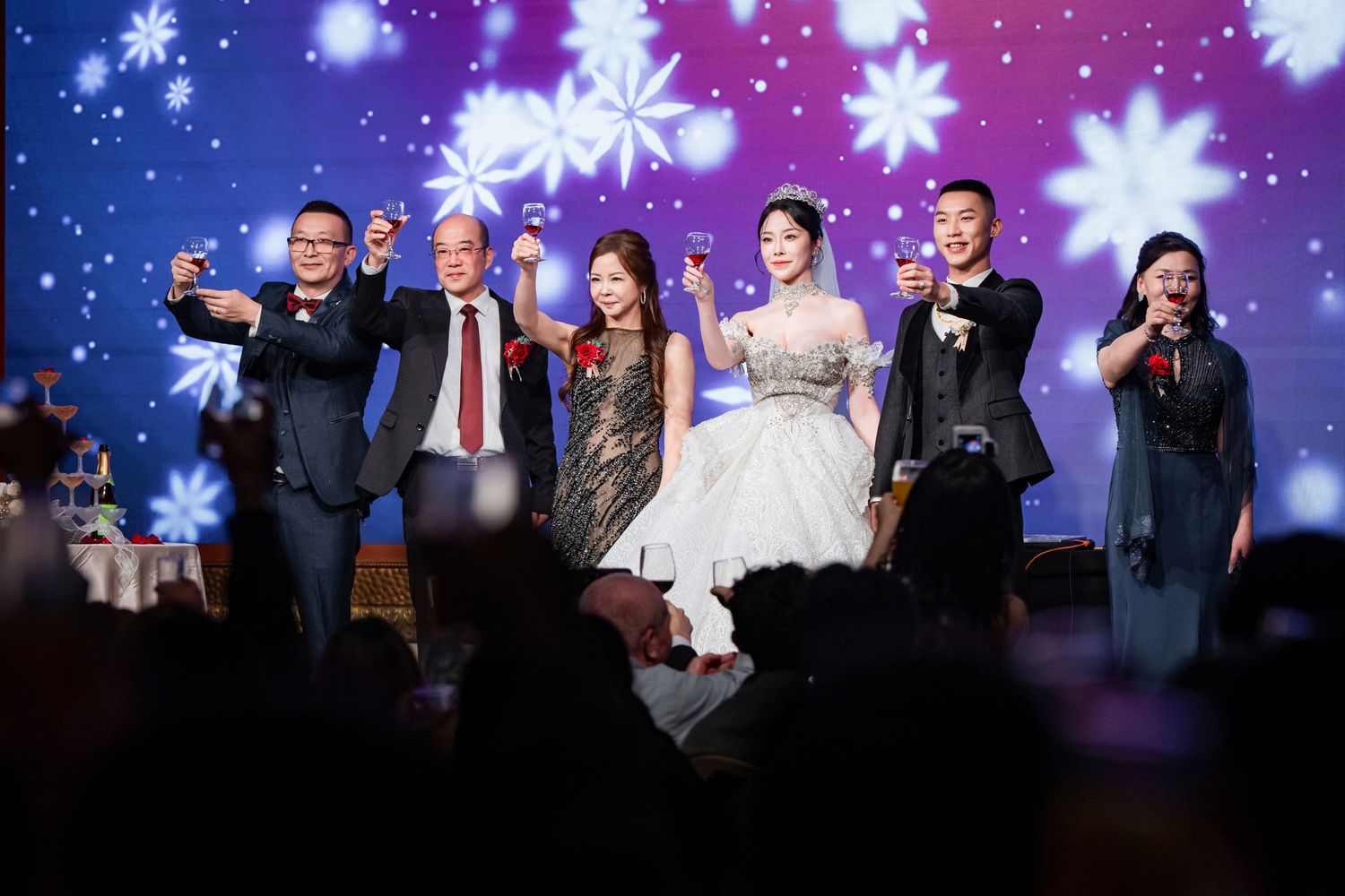 People celebrating and dancing on stage during a festive event with snowflake decorations and blue lighting effects.