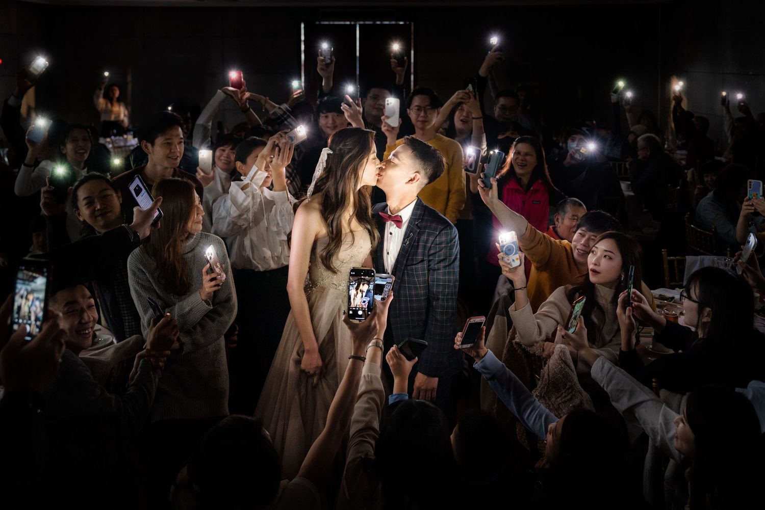 A crowd of people holding up illuminated phones at a nighttime event, capturing photos and videos in the darkness.
