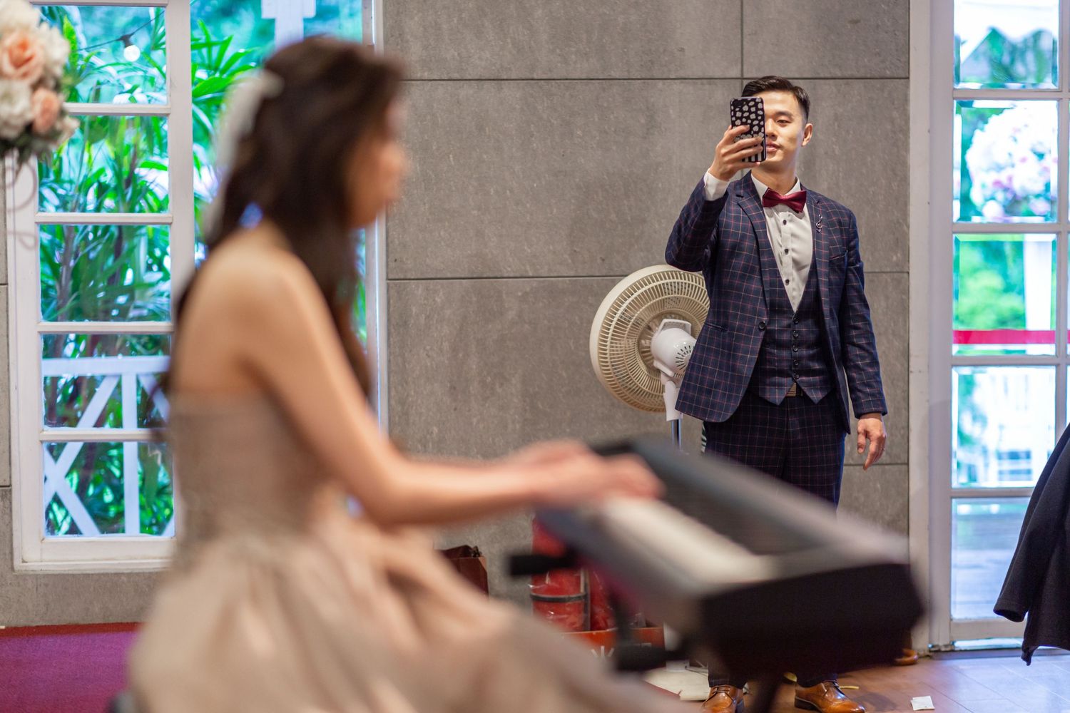 At a musical performance, someone in a suit takes a photo while a pianist plays on stage in elegant attire.