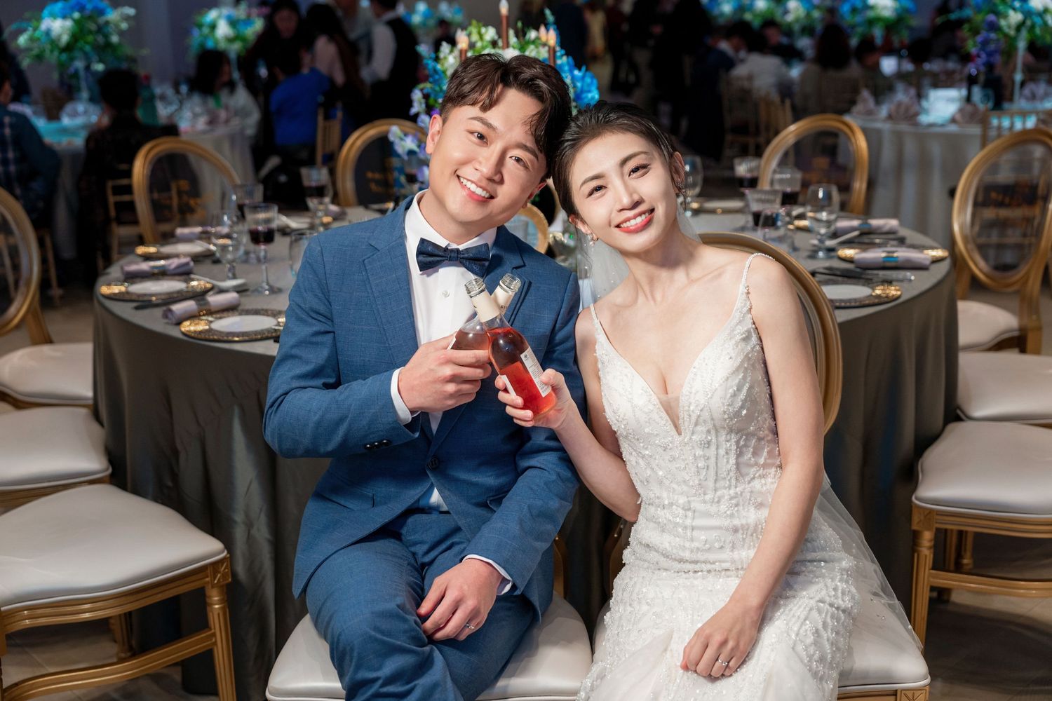 Wedding couple toasts with glasses at an elegant reception hall with decorated tables and chairs.