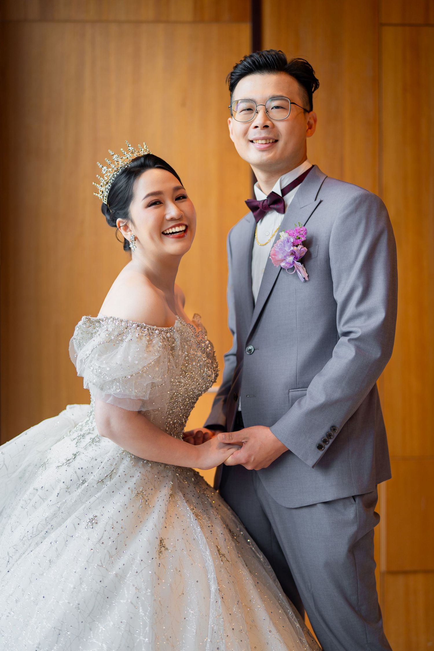 A bride in a sparkling ball gown and groom in grey suit share joyful candid moments together at their wedding.