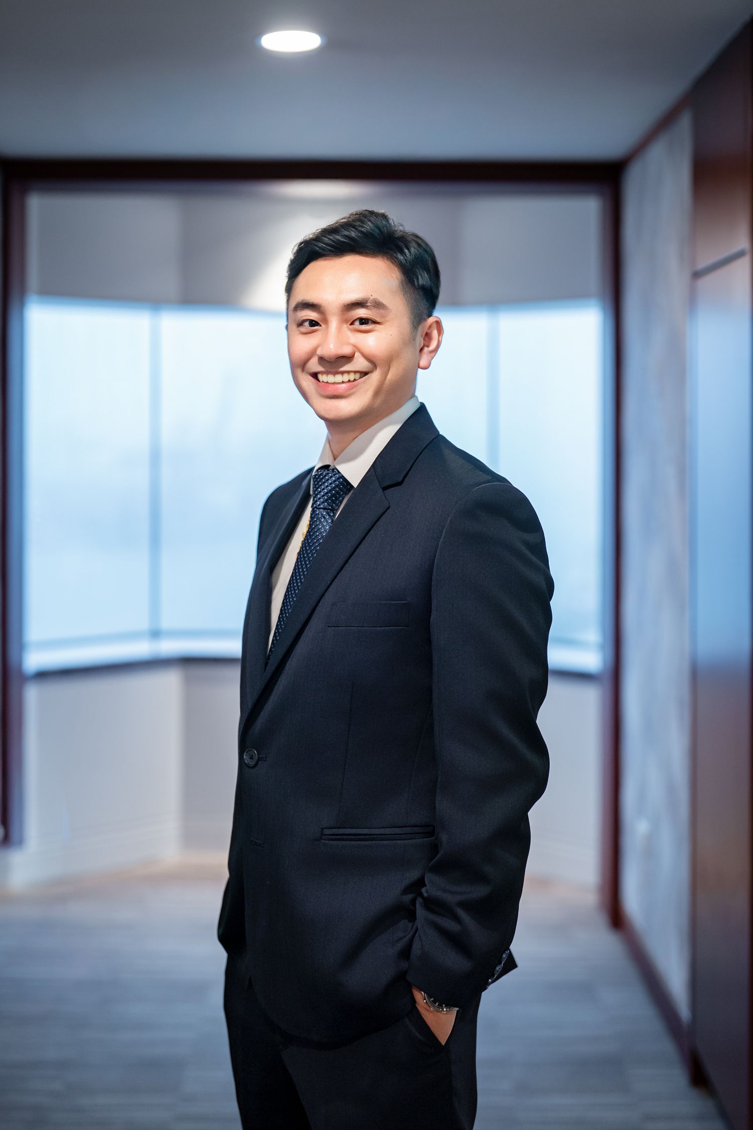 Professional in a black suit stands in a modern office hallway with natural lighting.