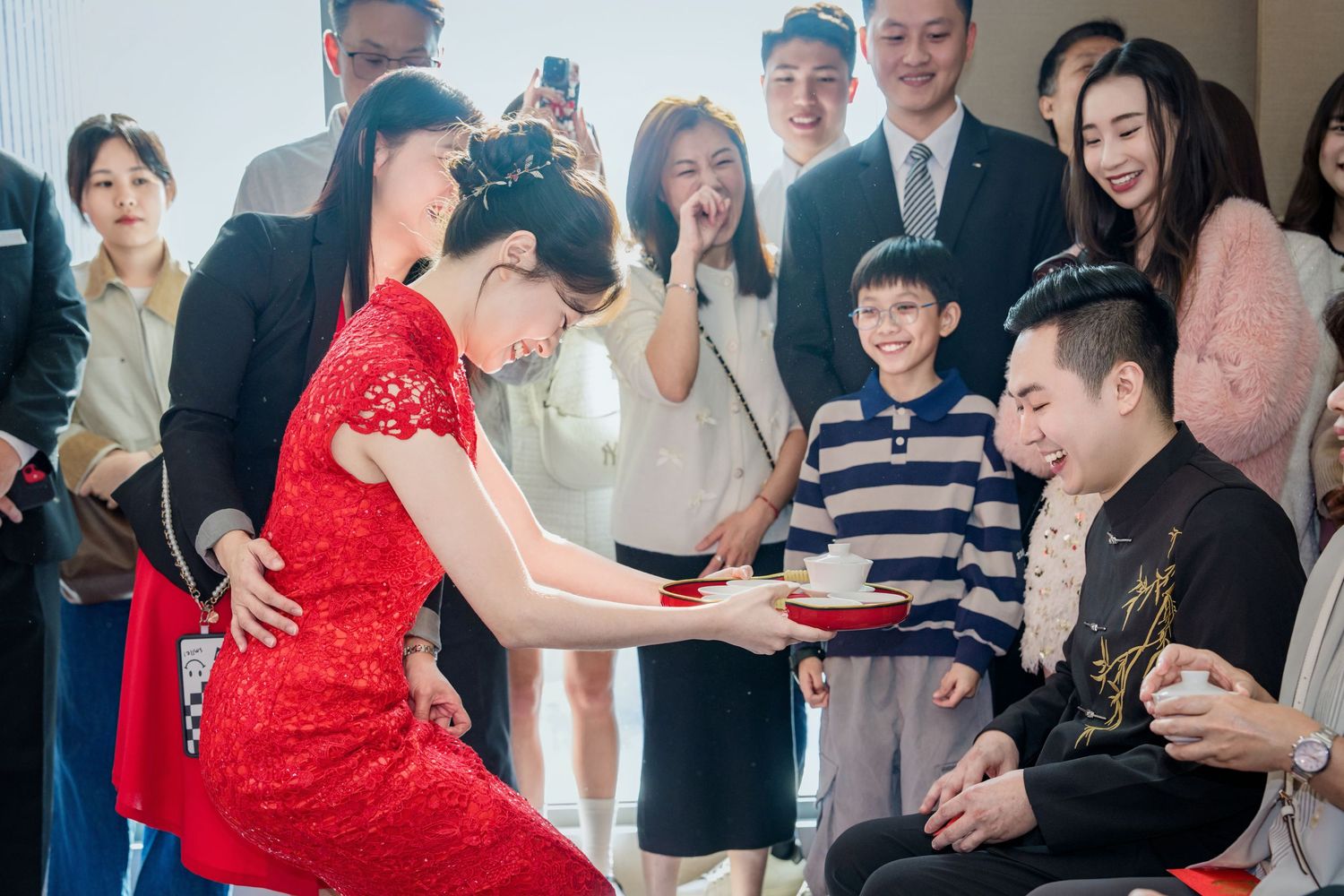 Wedding guests participate in a fun traditional Chinese tea ceremony game with red attire and laughter.