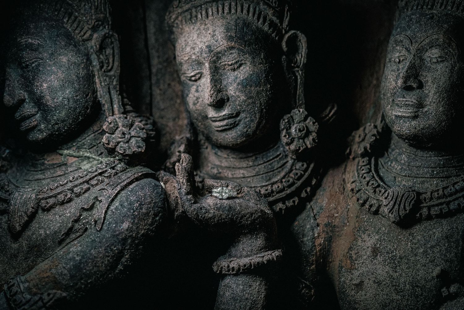 Ancient stone carved Hindu temple sculptures with intricate details, depicting deities in dark atmospheric lighting.