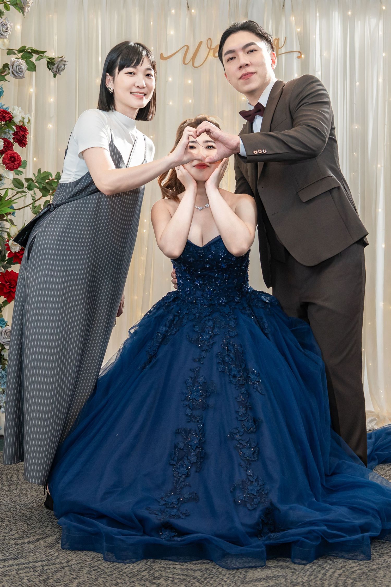 A couple in formal attire poses together, with the woman wearing an elegant navy blue ball gown with floral details.