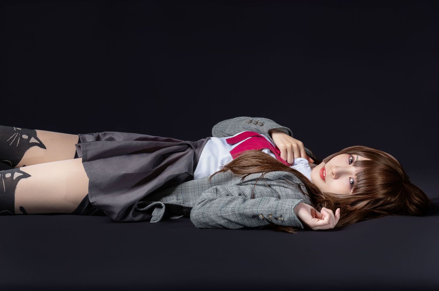A person lying on a dark surface wearing a gray sweater and black skirt in a dramatic pose against black background.