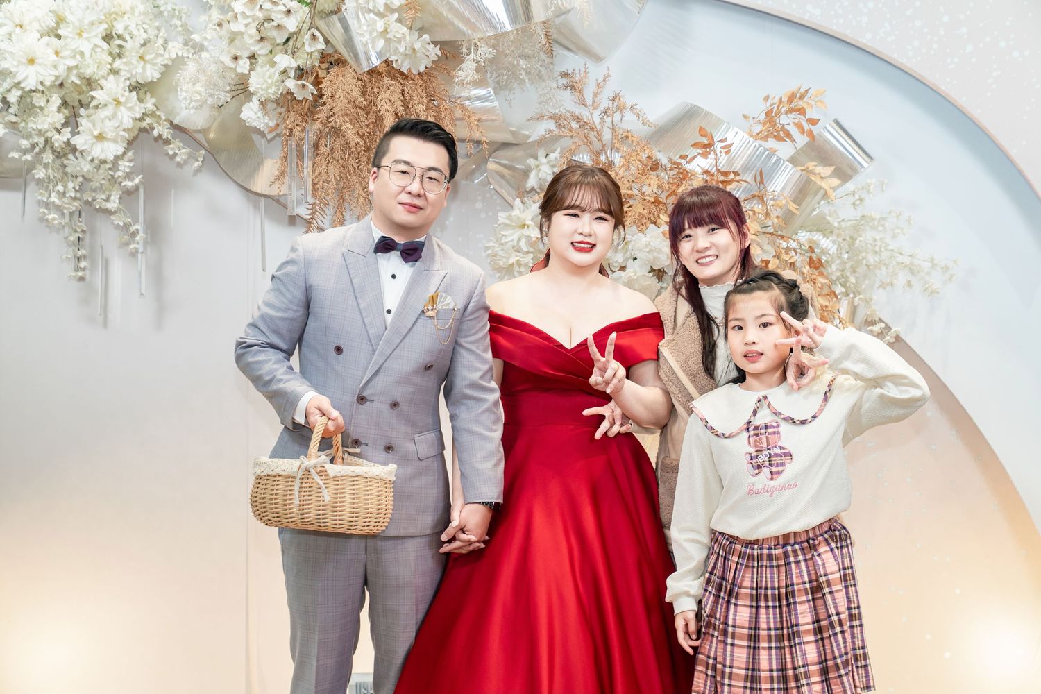 A family in coordinated formal attire poses together for holiday portraits against a white floral backdrop.
