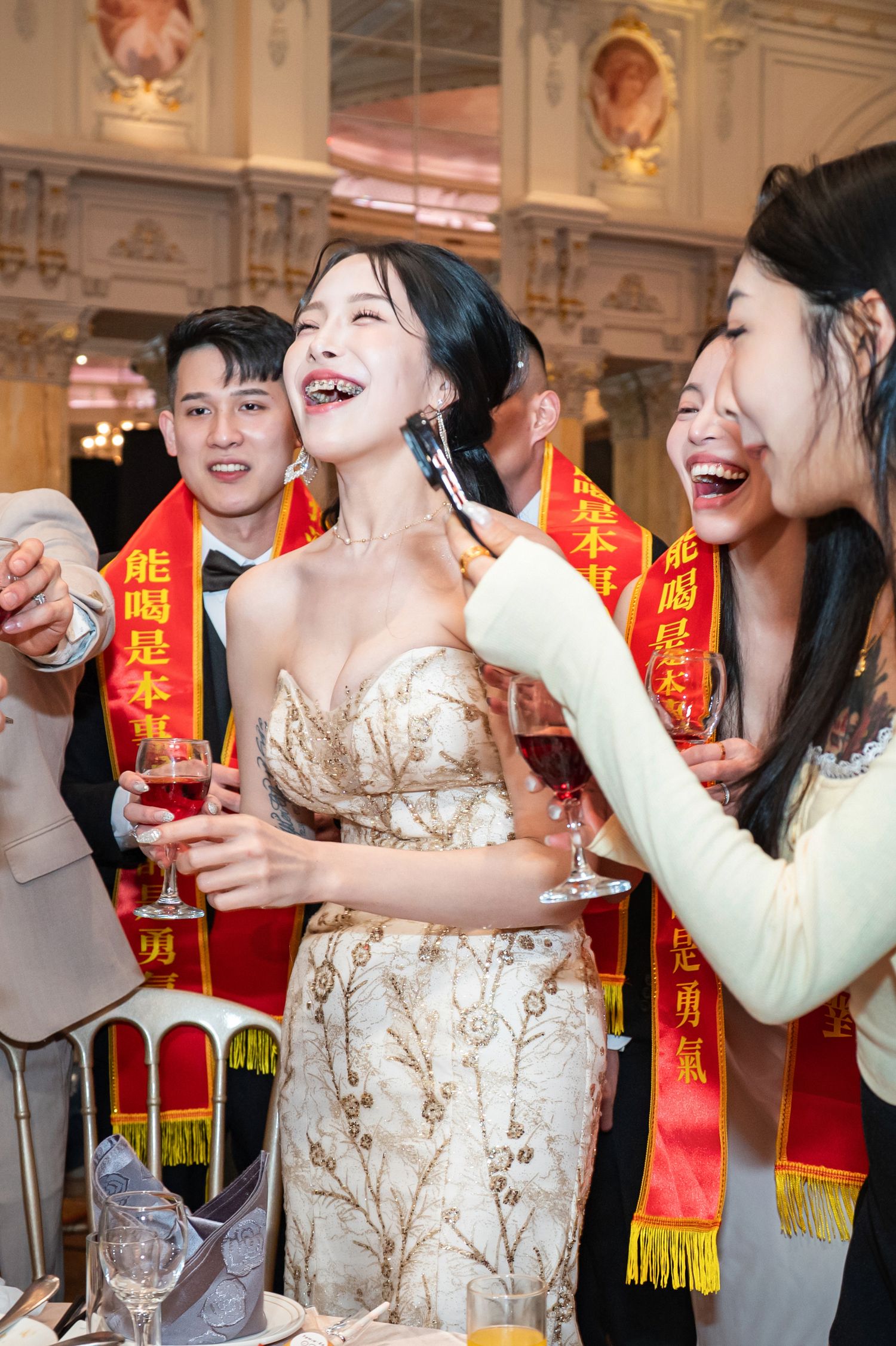 People celebrating at an elegant event with red and gold Chinese banners visible in an ornate venue.