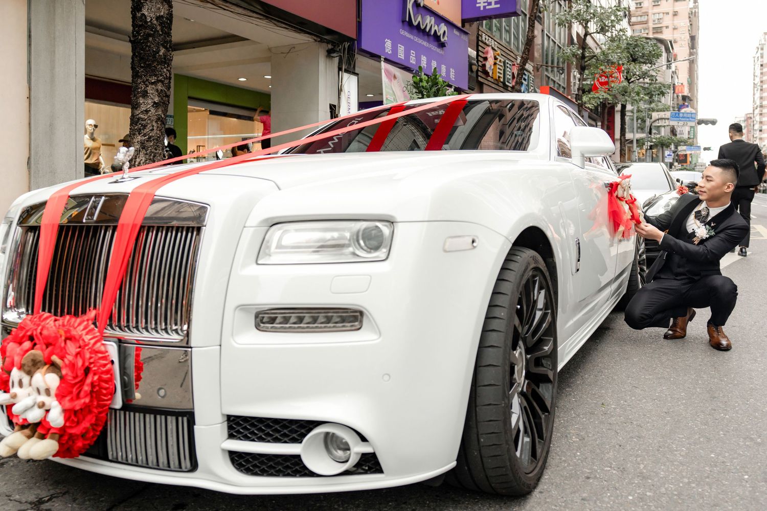 A white Rolls-Royce luxury car decorated with red ribbons and bows for a wedding celebration.