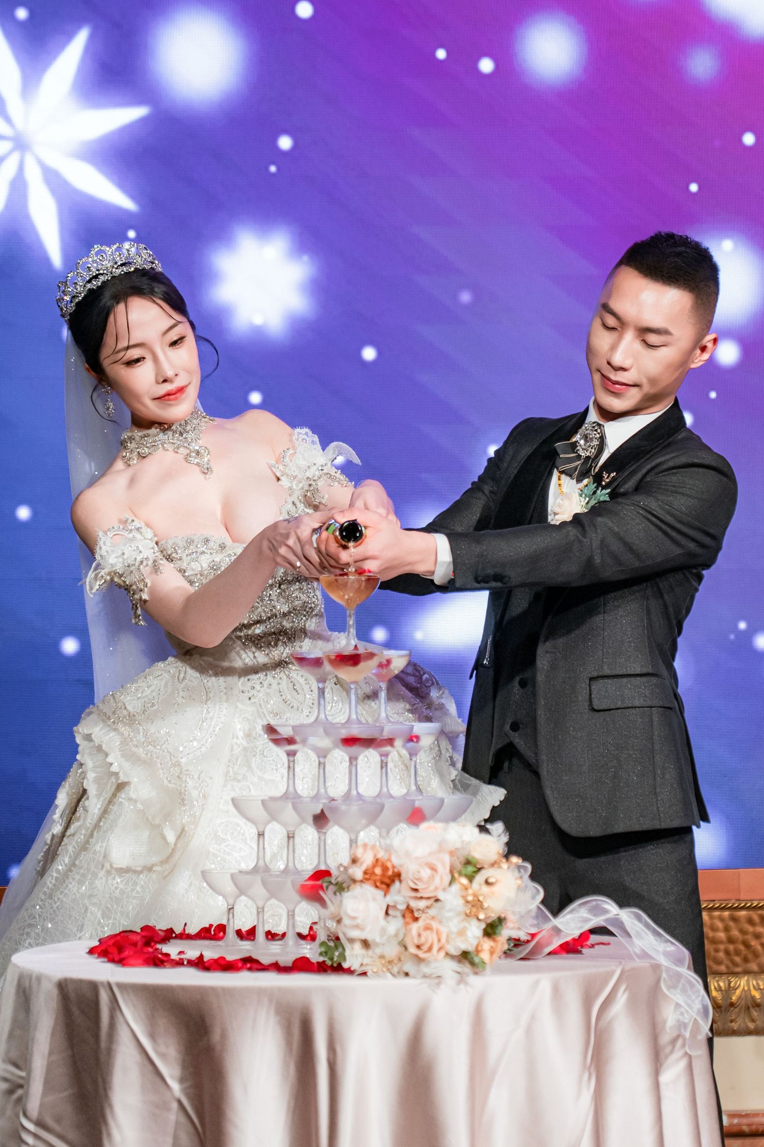 A bride and groom pour champagne into a tower of glasses at their wedding reception celebration.