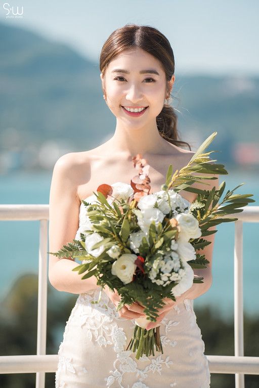 Bride holds elegant bouquet of white flowers and greenery on sunny outdoor terrace.