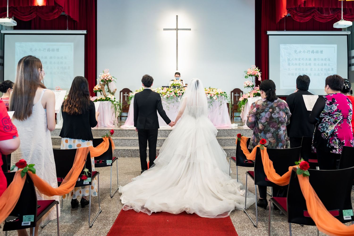 Church wedding ceremony with cross backdrop and orange aisle decorations.