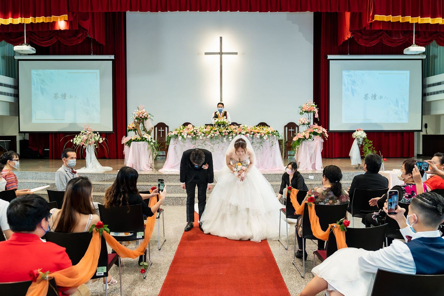 Church wedding ceremony with illuminated cross and red carpet leading to floral-decorated altar.