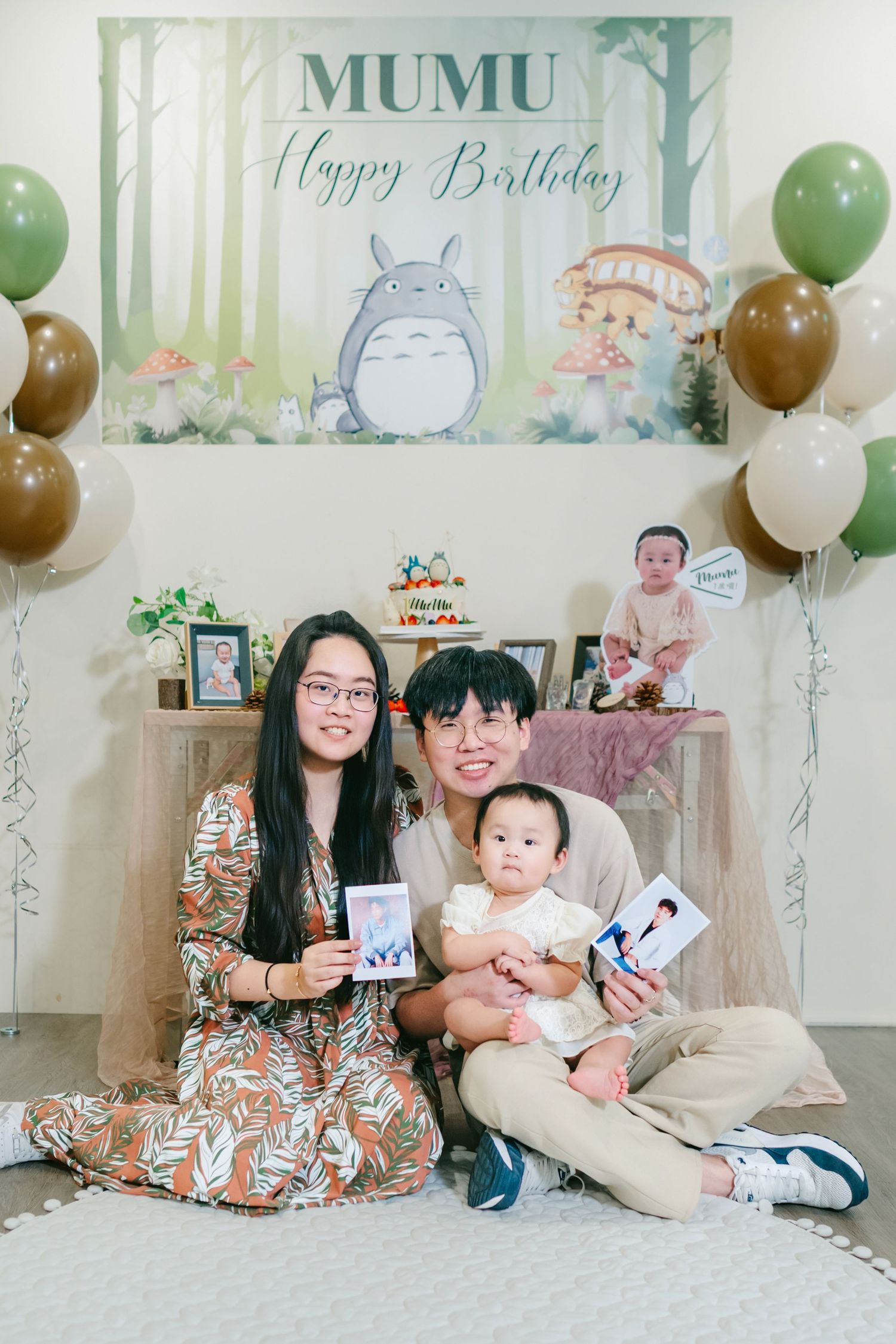 Birthday party setup with Totoro-themed backdrop, green and brown balloons, and party decorations against a white wall.