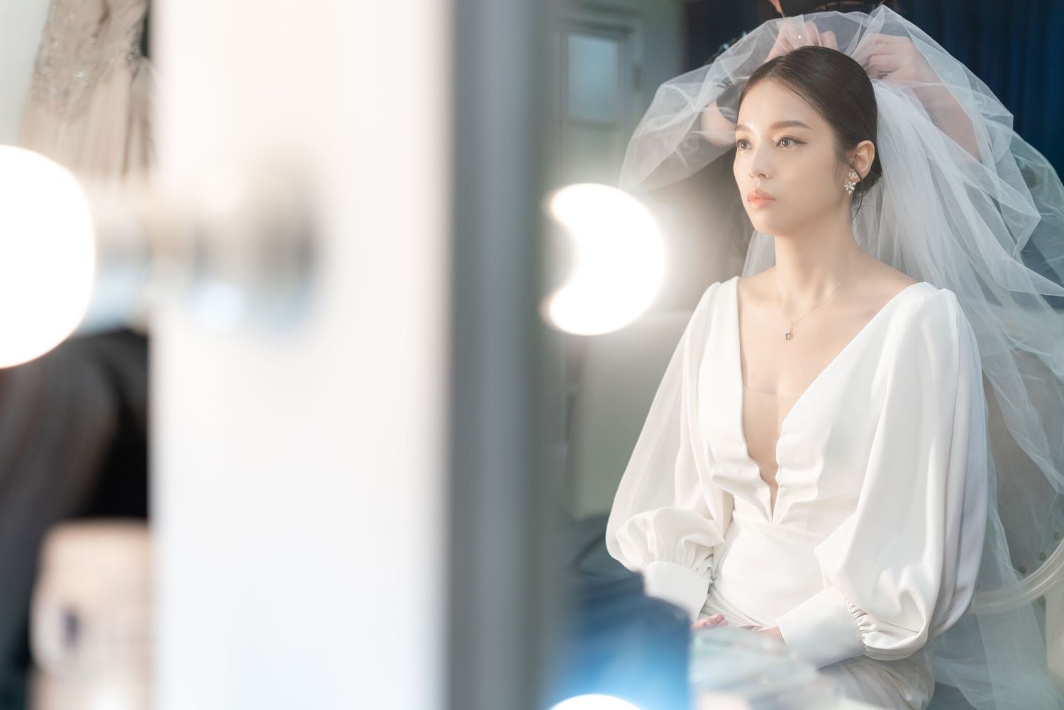 A bride in an elegant white wedding dress with billowing sleeves and veil poses in soft natural light.