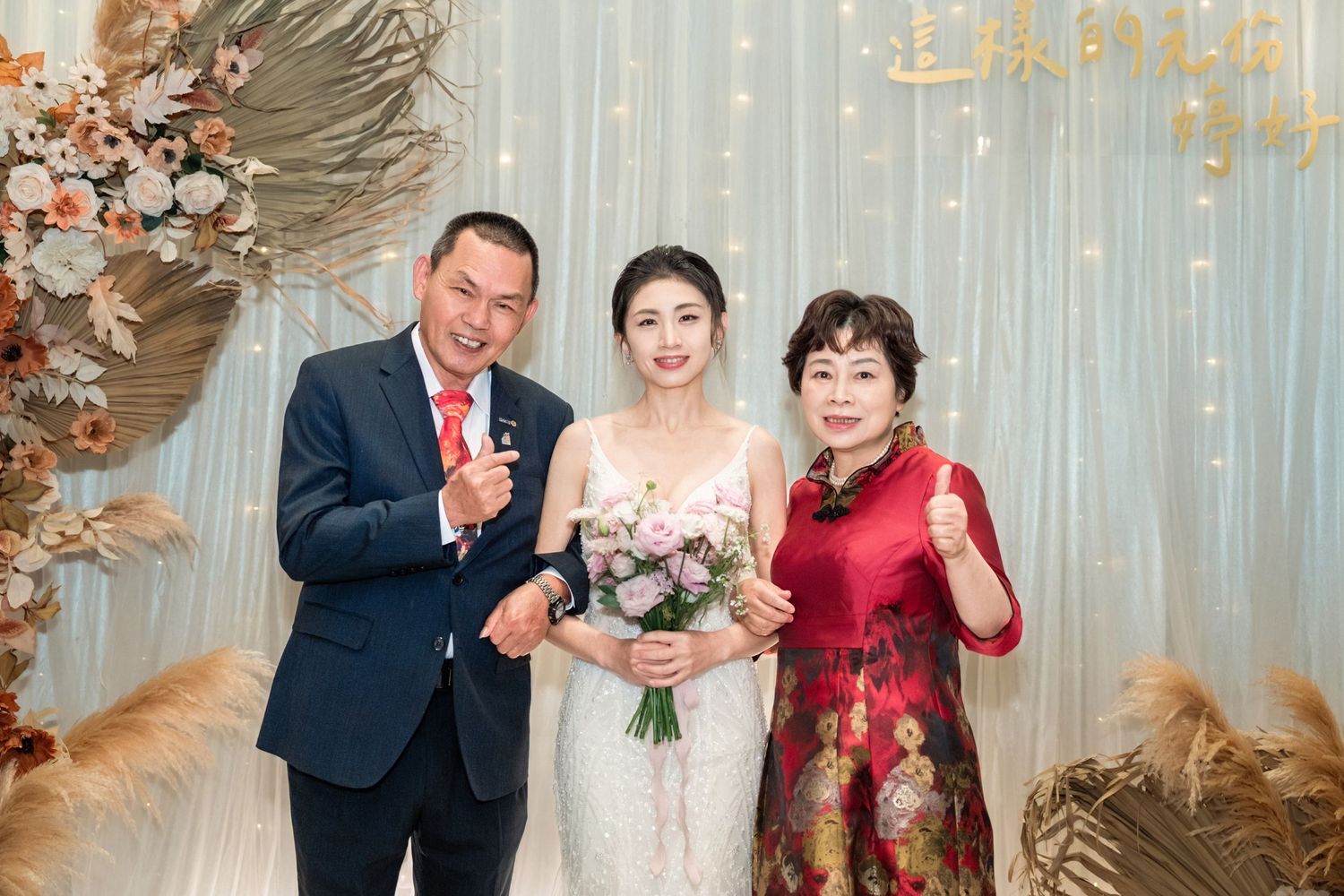 A wedding celebration with floral decorations and pampas grass arrangements against a shimmering backdrop.