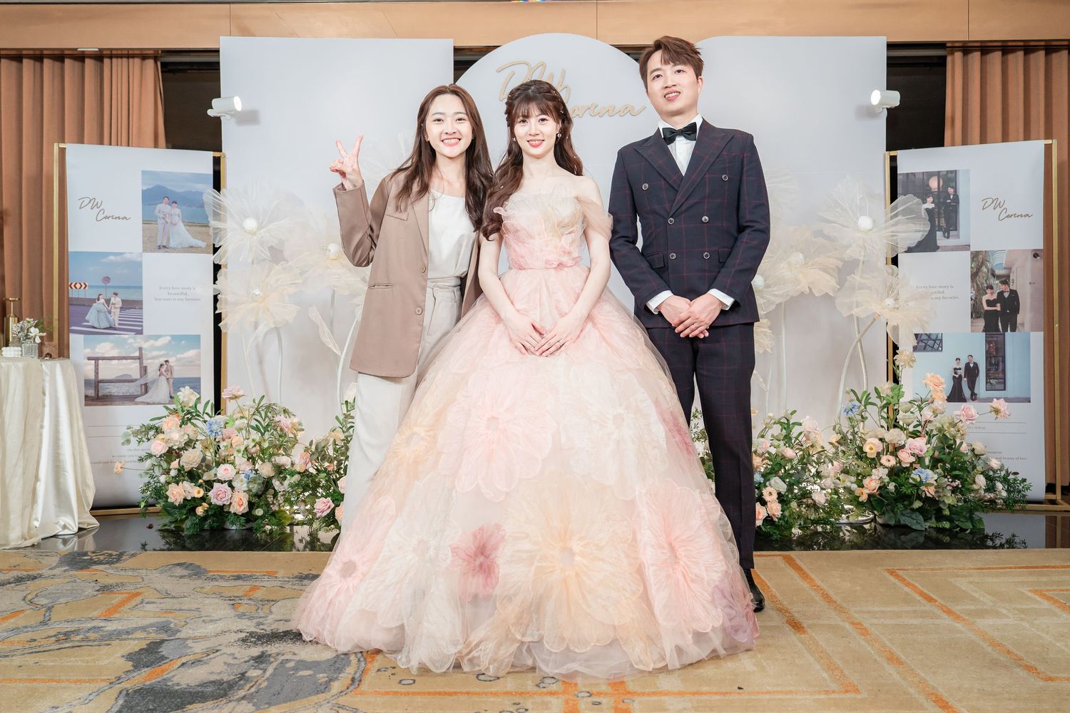 Three elegantly dressed people posing at a wedding reception, with a bride in a pink ball gown flanked by two guests.