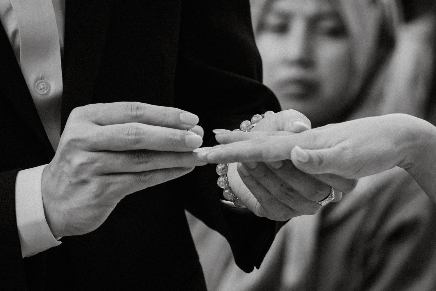 Black and white photo of groom placing wedding ring on brides finger during ceremony.