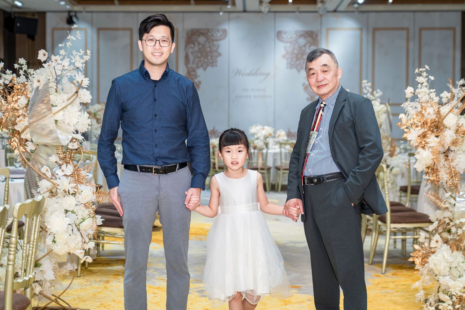 Three people stand together in an elegant wedding venue decorated with dried floral arrangements and gold accents.