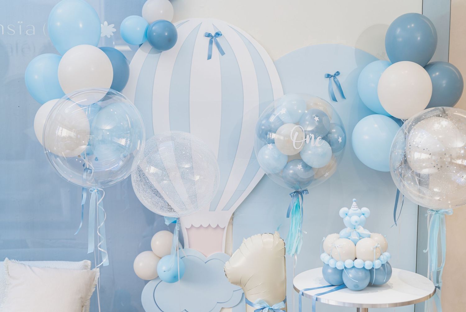 Blue and white balloon garland decorates a festive party space with elegant table settings and pastel accents.