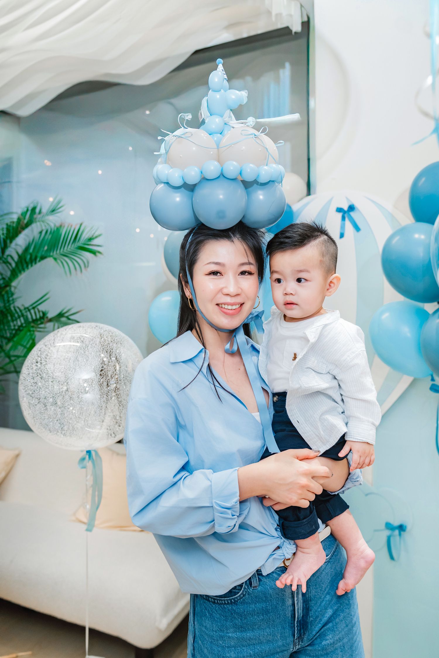 A baby shower celebration setup with blue balloon decorations and white furniture in a modern interior space.
