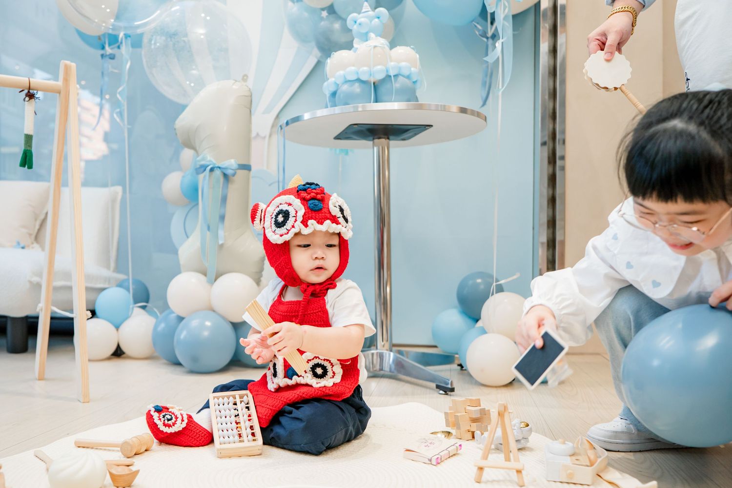 A baby shower celebration with blue and white balloon decorations and stuffed animals in a modern indoor setting.